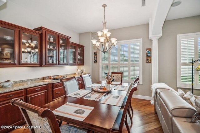 dining room with ornate columns, hardwood / wood-style floors, and an inviting chandelier