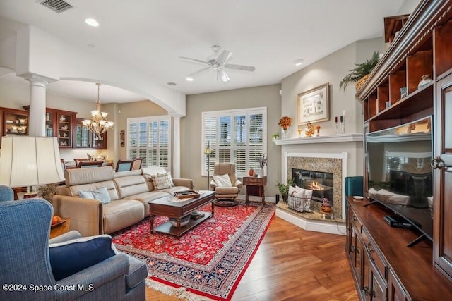 living room featuring decorative columns, a fireplace, hardwood / wood-style floors, and ceiling fan with notable chandelier