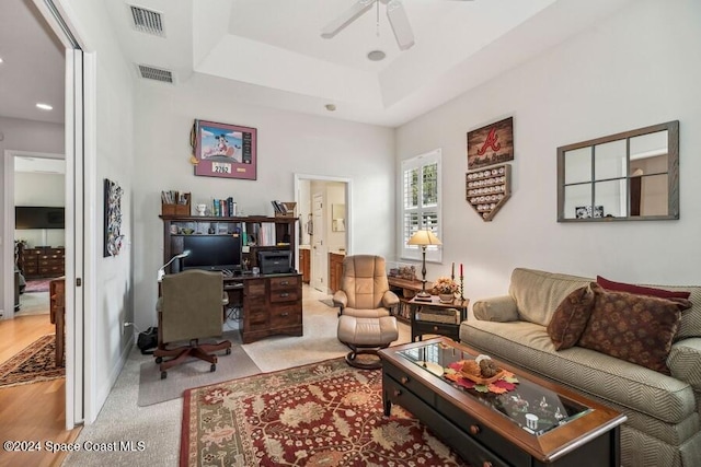 living room with ceiling fan, a raised ceiling, and light hardwood / wood-style flooring