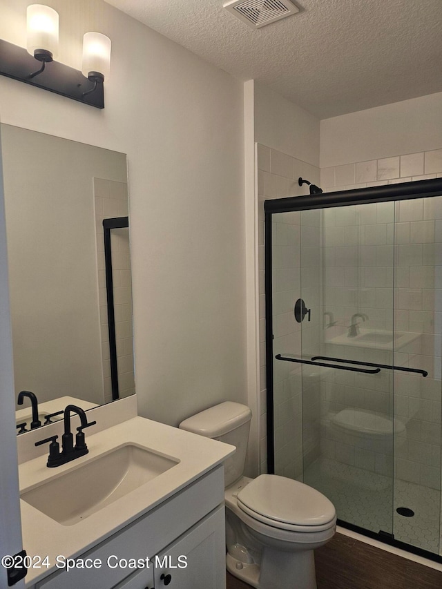 bathroom featuring wood-type flooring, toilet, a textured ceiling, an enclosed shower, and vanity