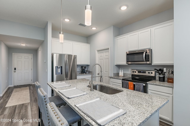 kitchen with a center island with sink, white cabinets, hanging light fixtures, sink, and appliances with stainless steel finishes