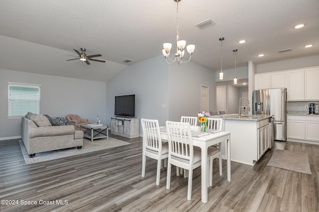 dining space featuring ceiling fan with notable chandelier, a textured ceiling, dark wood-type flooring, sink, and lofted ceiling