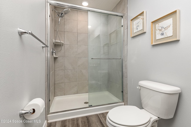 bathroom with hardwood / wood-style floors, a shower with shower door, and toilet