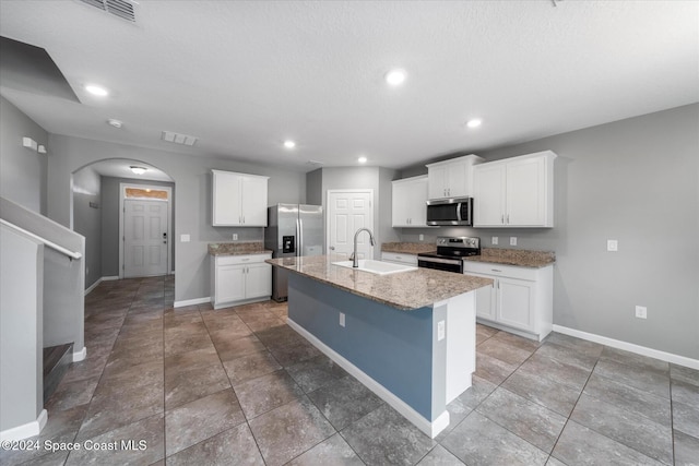 kitchen featuring stainless steel appliances, white cabinets, sink, an island with sink, and light stone countertops