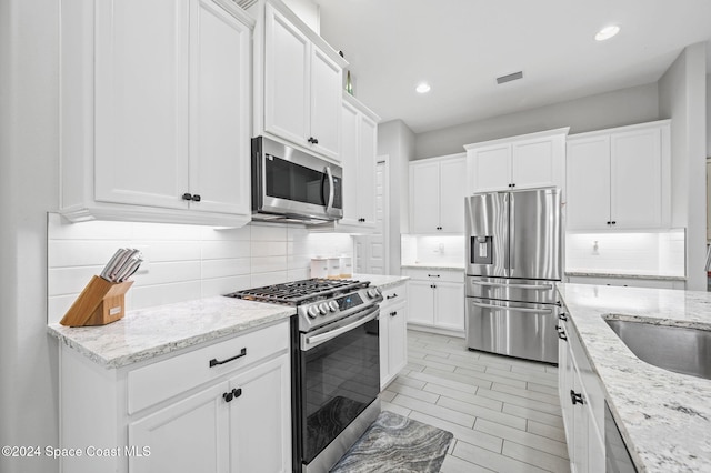 kitchen featuring white cabinets, appliances with stainless steel finishes, tasteful backsplash, and light stone countertops