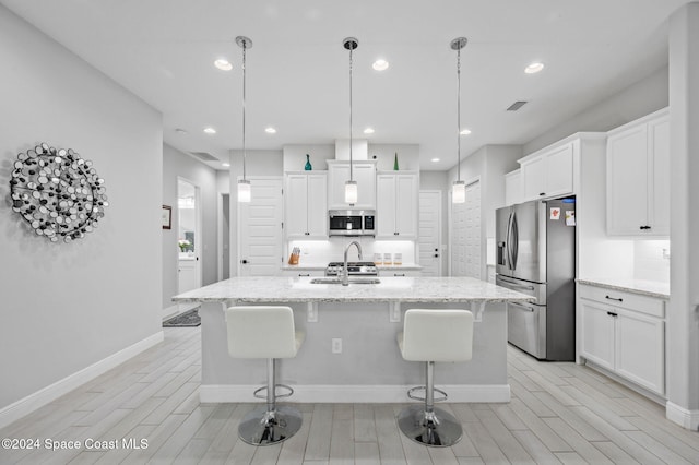 kitchen with stainless steel appliances, light stone counters, decorative light fixtures, and an island with sink