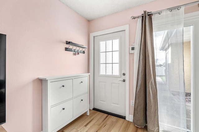 doorway to outside with a textured ceiling and light hardwood / wood-style flooring