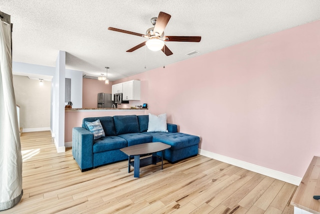 living room with ceiling fan, a textured ceiling, and light hardwood / wood-style flooring