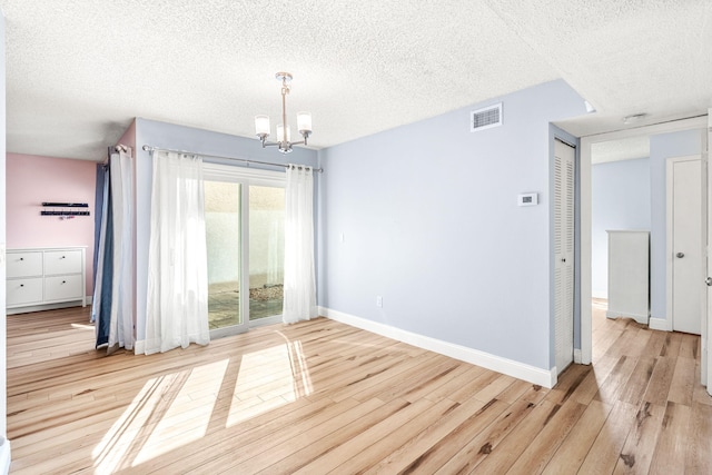 spare room featuring a chandelier, a textured ceiling, and light wood-type flooring