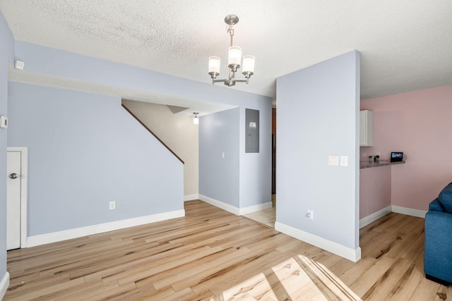 interior space with electric panel, light hardwood / wood-style flooring, a textured ceiling, and a notable chandelier