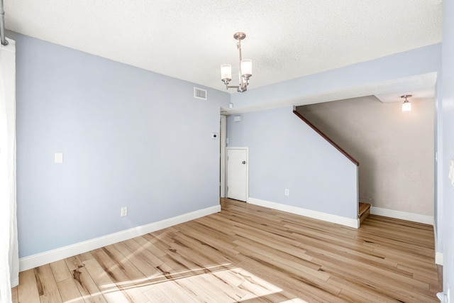 unfurnished room featuring light hardwood / wood-style floors, a textured ceiling, and an inviting chandelier