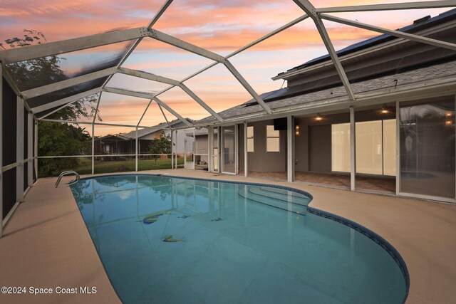 pool at dusk featuring a lanai and a patio area