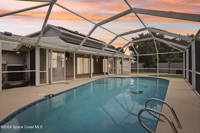 pool at dusk featuring a lanai, a patio area, and central AC