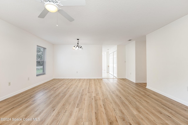 empty room featuring ceiling fan with notable chandelier, a textured ceiling, and light hardwood / wood-style flooring