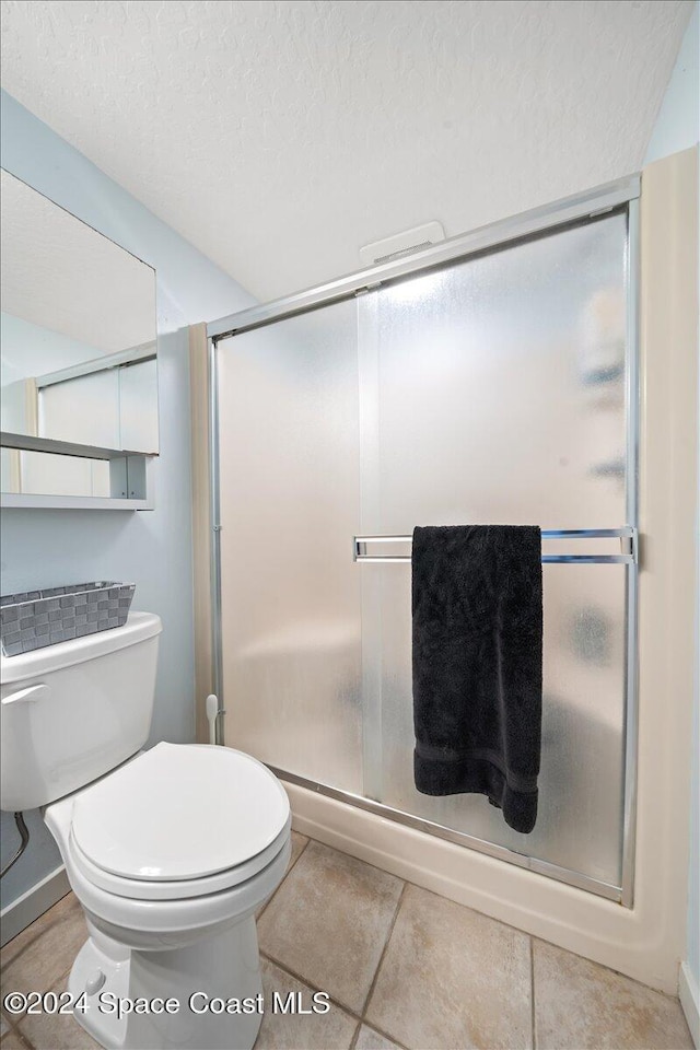 bathroom featuring tile patterned floors, toilet, a shower with shower door, and a textured ceiling