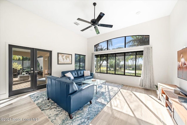 living room with french doors, a towering ceiling, light hardwood / wood-style flooring, and ceiling fan