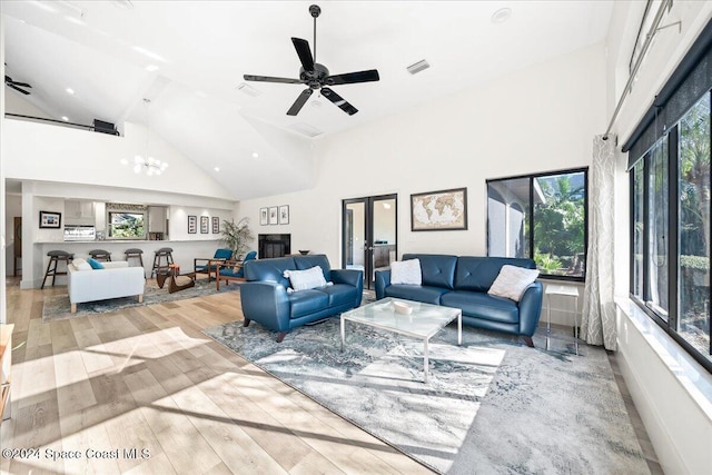 living room with beamed ceiling, ceiling fan with notable chandelier, light wood-type flooring, and high vaulted ceiling