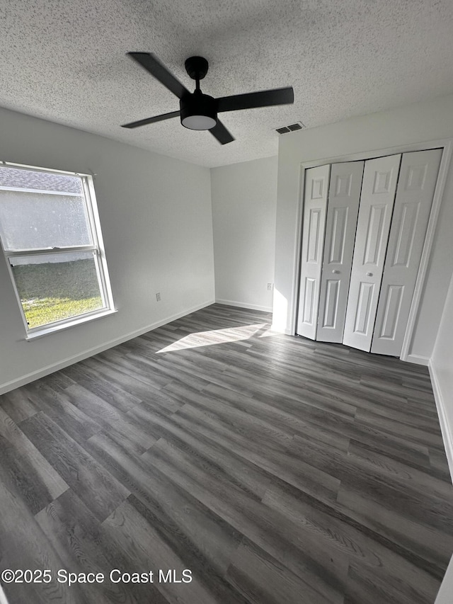 unfurnished bedroom featuring ceiling fan, dark hardwood / wood-style flooring, a textured ceiling, and a closet