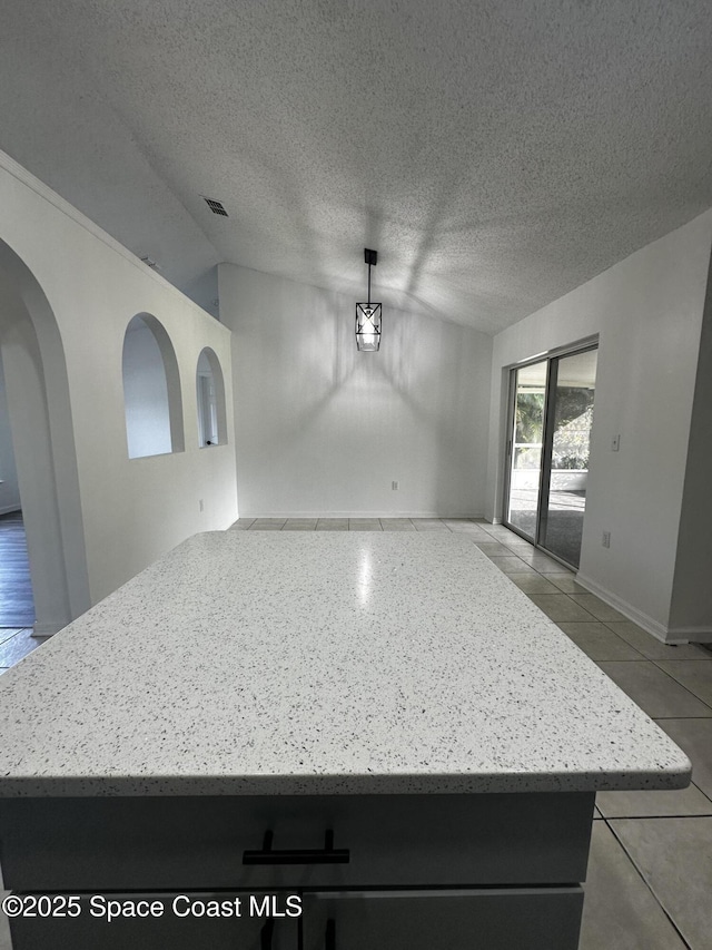 kitchen with light tile patterned flooring, light stone counters, hanging light fixtures, and vaulted ceiling