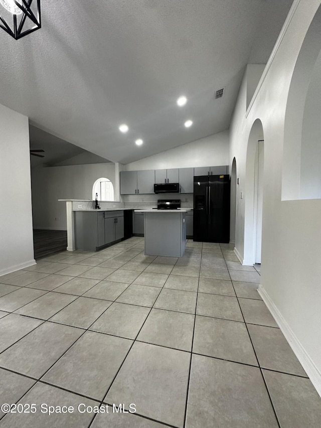 kitchen with gray cabinetry, a kitchen island, lofted ceiling, light tile patterned floors, and black appliances