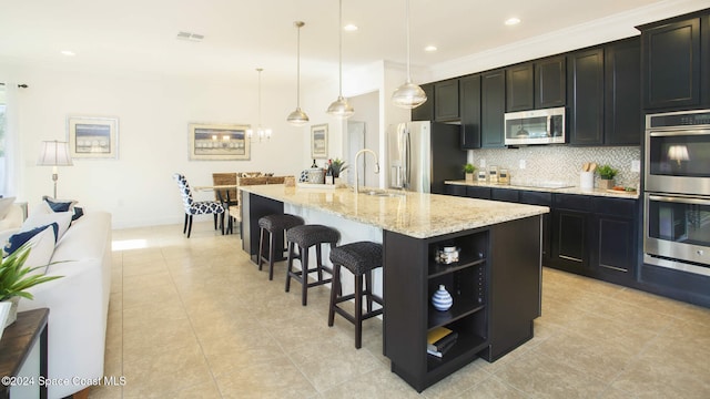 kitchen with stainless steel appliances, tasteful backsplash, a kitchen breakfast bar, hanging light fixtures, and a kitchen island with sink