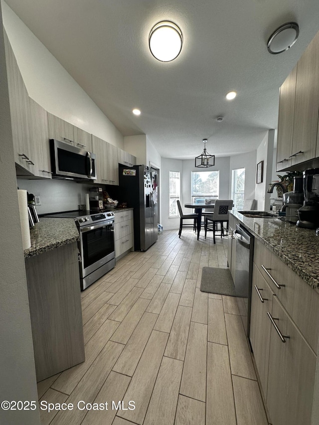 kitchen with appliances with stainless steel finishes, dark stone counters, sink, pendant lighting, and an inviting chandelier