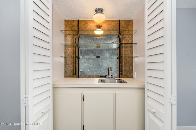 bar featuring white cabinets, sink, and a textured ceiling