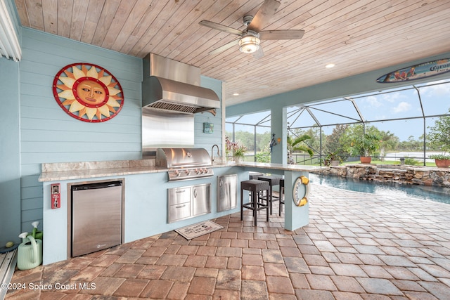 view of patio with pool water feature, glass enclosure, area for grilling, and an outdoor wet bar