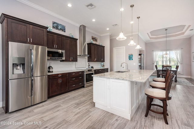 kitchen with appliances with stainless steel finishes, light hardwood / wood-style floors, a kitchen island with sink, and wall chimney range hood