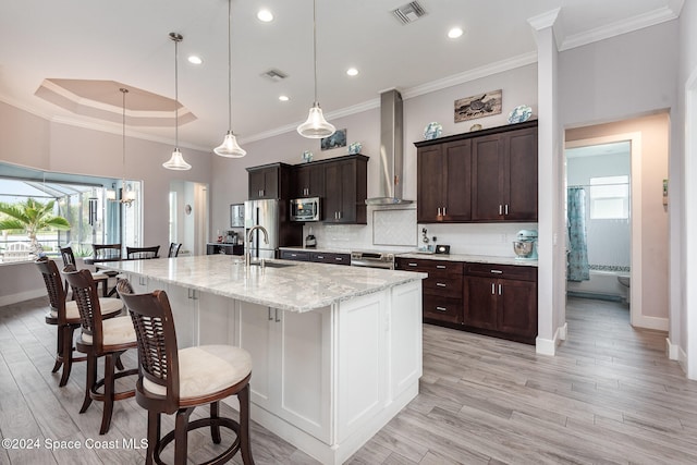 kitchen featuring wall chimney exhaust hood, crown molding, sink, light hardwood / wood-style flooring, and hanging light fixtures