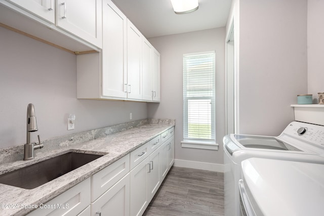 laundry room with washing machine and clothes dryer, light wood-type flooring, cabinets, and sink