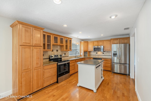 kitchen with appliances with stainless steel finishes, sink, light hardwood / wood-style floors, and a center island