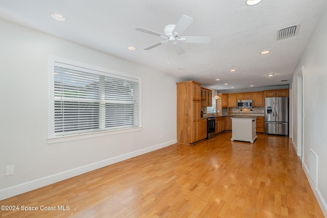 kitchen featuring light wood-type flooring, ceiling fan, a kitchen island, and appliances with stainless steel finishes