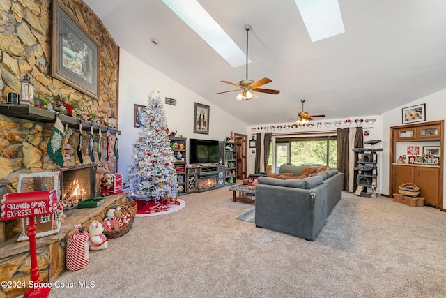 carpeted living room with a skylight, ceiling fan, a stone fireplace, and high vaulted ceiling