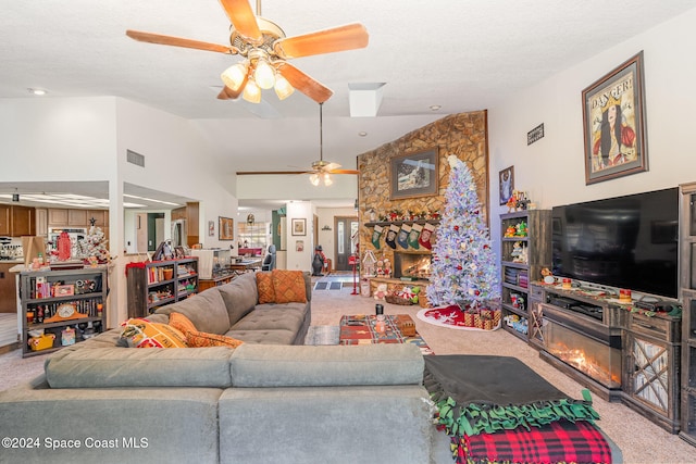 carpeted living room with ceiling fan, a stone fireplace, and vaulted ceiling