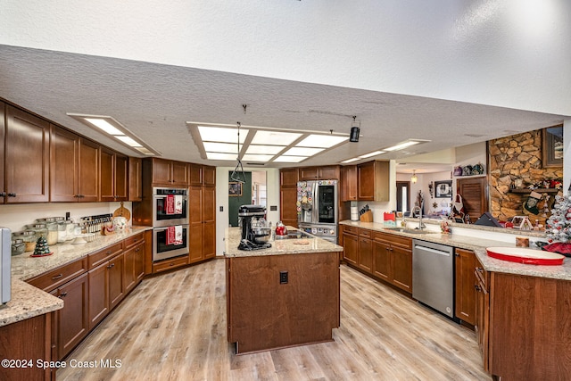 kitchen with sink, kitchen peninsula, light hardwood / wood-style floors, a textured ceiling, and appliances with stainless steel finishes