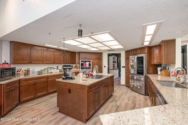 kitchen with light stone countertops, appliances with stainless steel finishes, light wood-type flooring, a textured ceiling, and sink