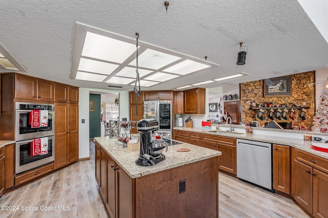 kitchen featuring appliances with stainless steel finishes, a textured ceiling, sink, light hardwood / wood-style flooring, and a kitchen island