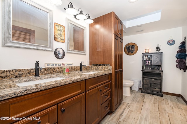 bathroom with hardwood / wood-style flooring, vanity, toilet, and a skylight