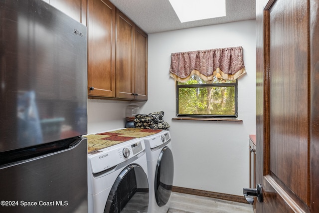 laundry area with cabinets, light hardwood / wood-style floors, washing machine and dryer, and a textured ceiling