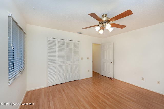 unfurnished bedroom with a textured ceiling, light hardwood / wood-style flooring, a closet, and ceiling fan