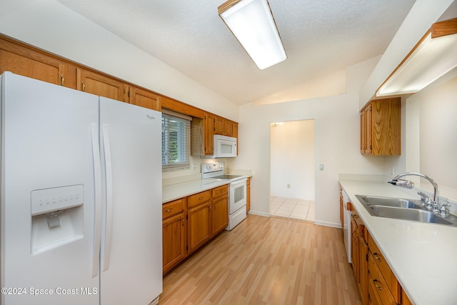 kitchen featuring vaulted ceiling, white appliances, sink, and light wood-type flooring