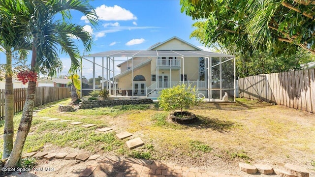 back of property with glass enclosure, a lawn, french doors, and a balcony