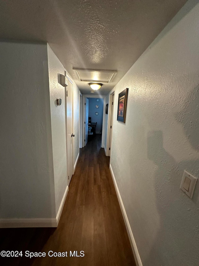 corridor with dark hardwood / wood-style flooring and a textured ceiling