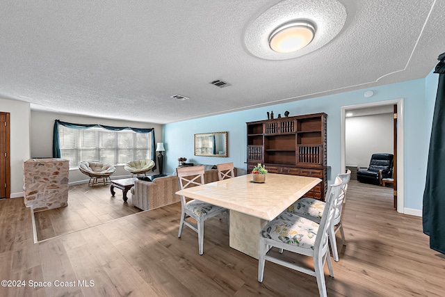 dining area featuring light wood-type flooring and a textured ceiling