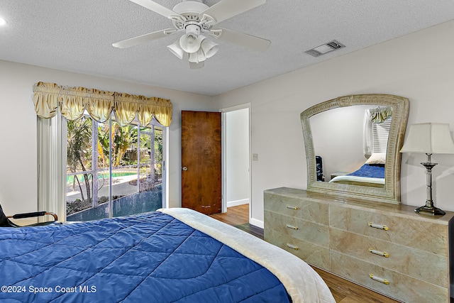 bedroom with access to exterior, ceiling fan, wood-type flooring, and a textured ceiling