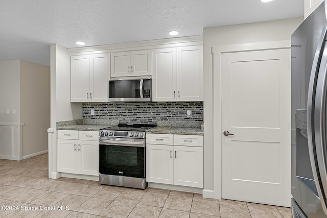 kitchen featuring light stone countertops, backsplash, stainless steel appliances, and white cabinetry