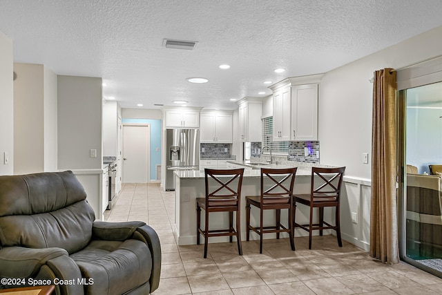 kitchen with kitchen peninsula, a breakfast bar, a textured ceiling, stainless steel appliances, and white cabinetry