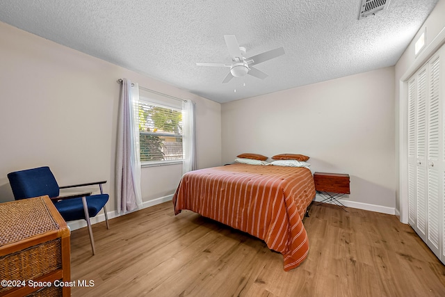 bedroom with ceiling fan, a closet, light hardwood / wood-style floors, and a textured ceiling