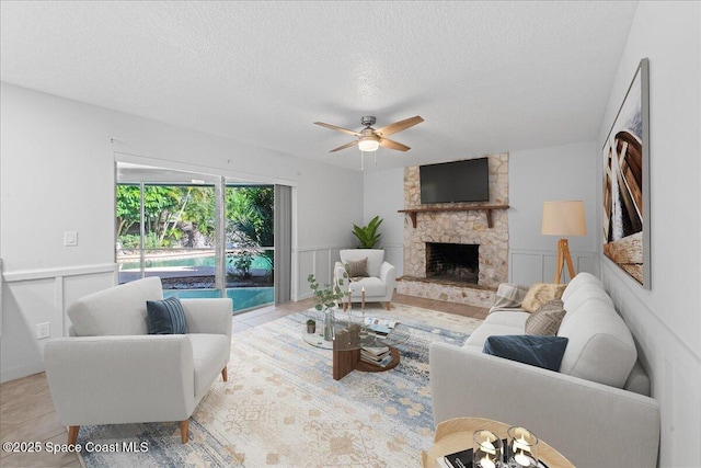 560 Rio Ln, Indialantic, FL 32903 - living room with ceiling fan, a textured ceiling, a decorative wall, a stone fireplace, and a wainscoted wall